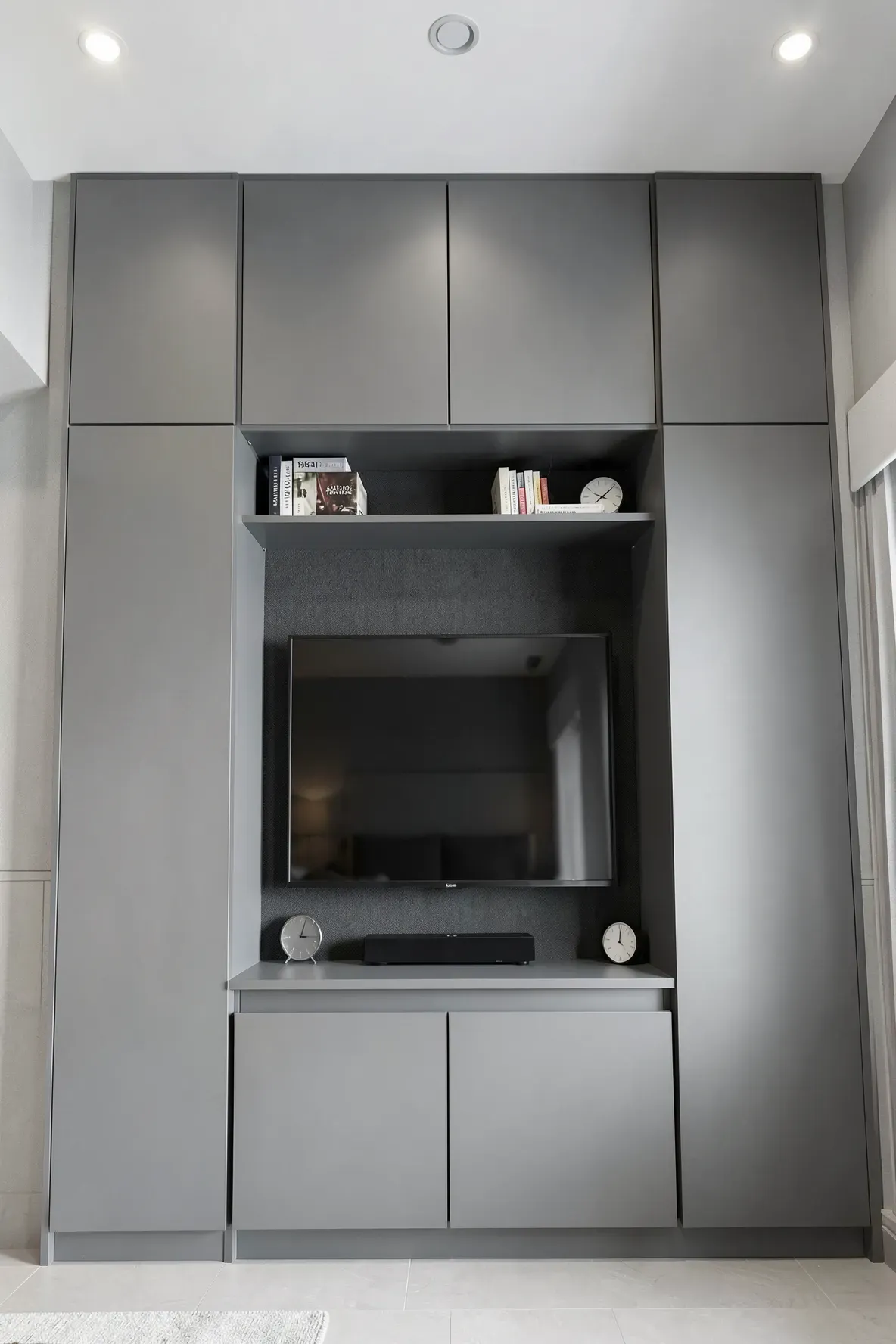 A floor-to-ceiling matte grey wardrobe with storage cabinets above a central television.