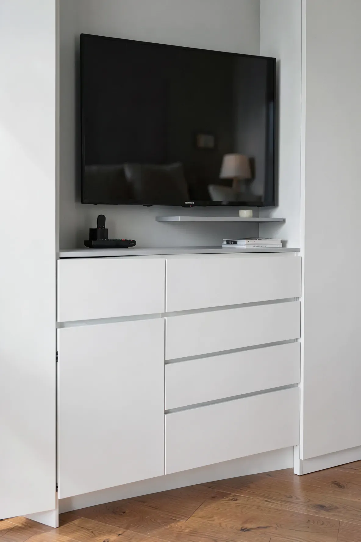 Sleek white soft-close drawers built into a wardrobe directly underneath a television screen.