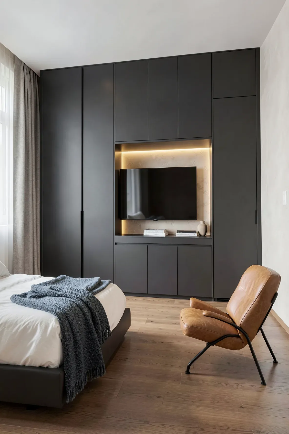 A modern bedroom with a grey built-in wardrobe featuring pocket doors that slide back to reveal a TV.