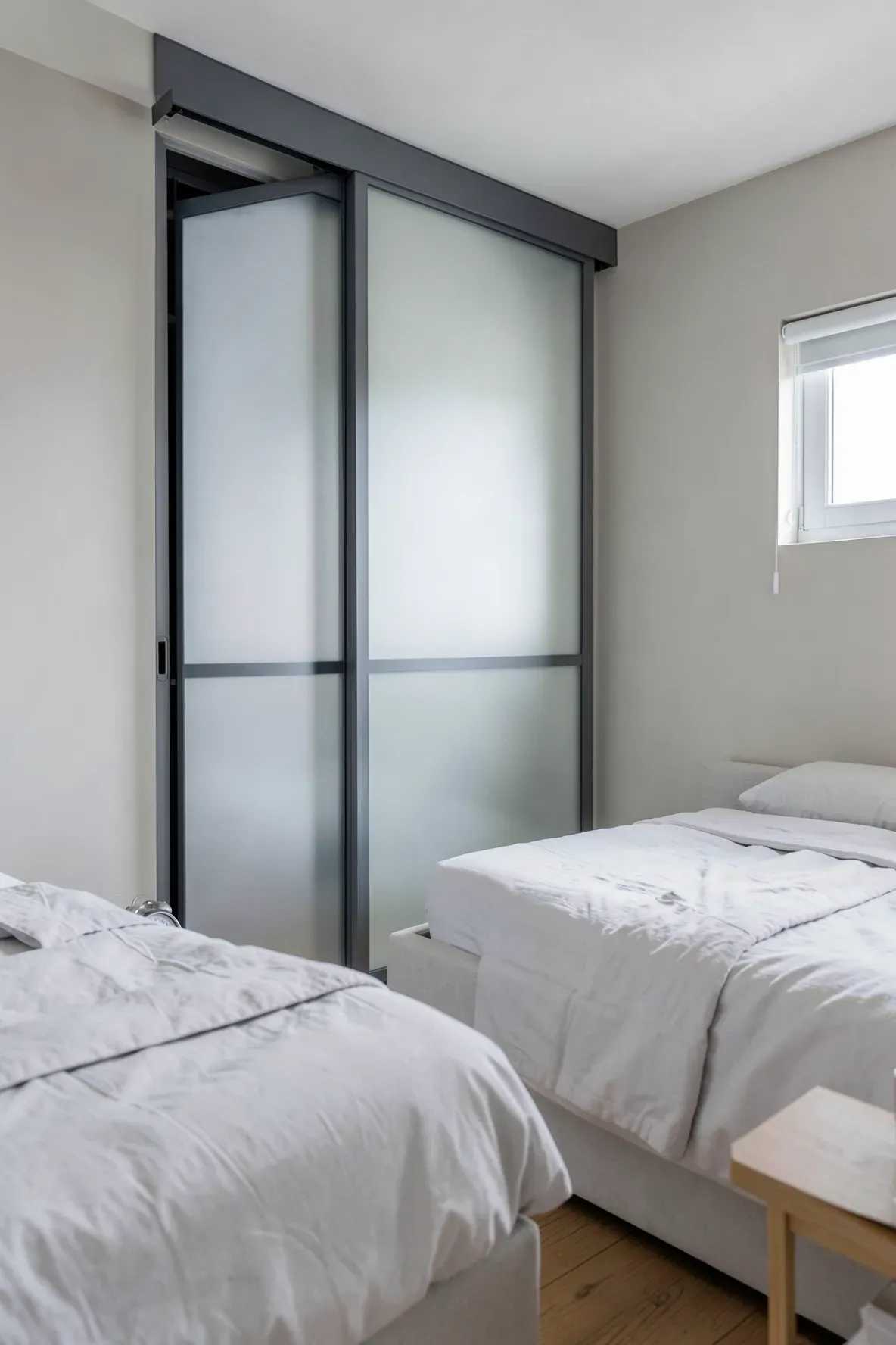 A narrow bedroom with a sliding door wardrobe featuring frosted glass panels next to the bed.