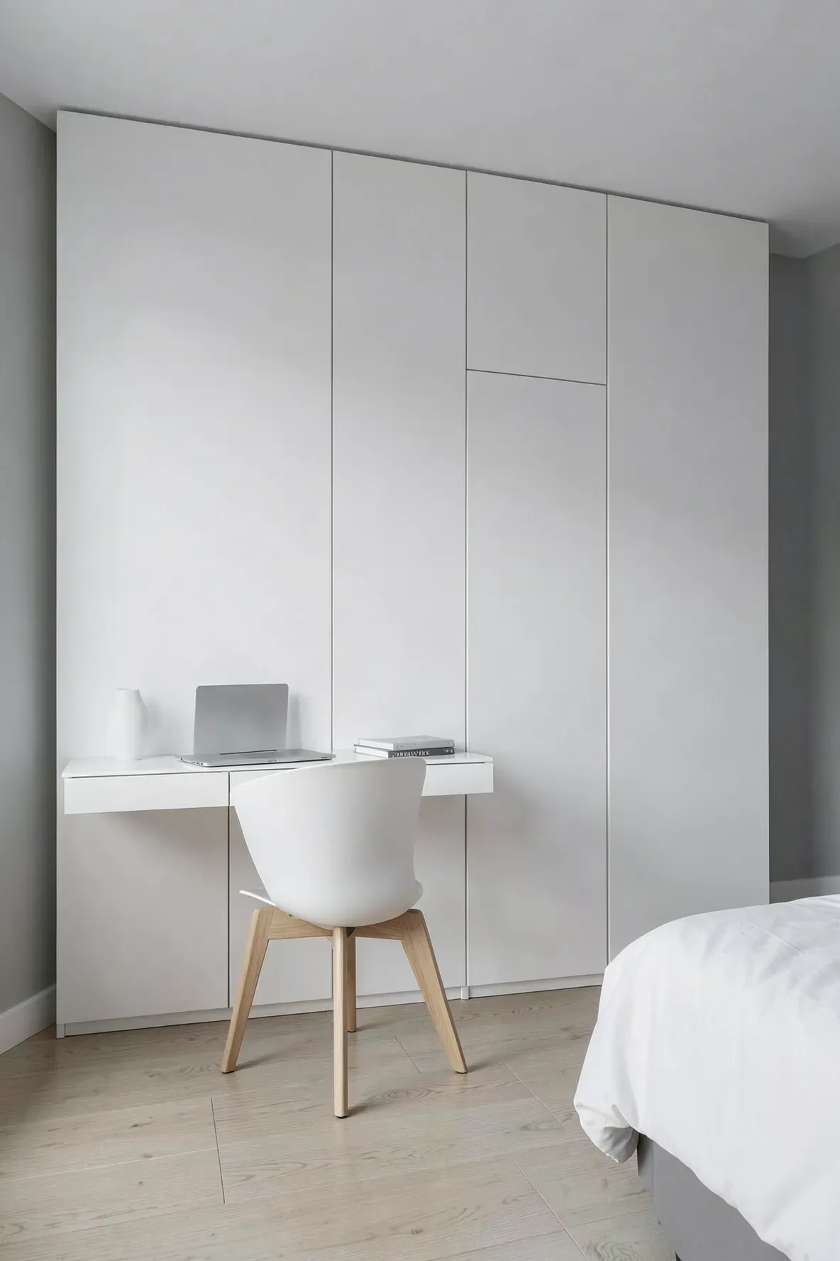 A seamless white minimalist wardrobe with a built-in desk and a modern chair in a bright room.
