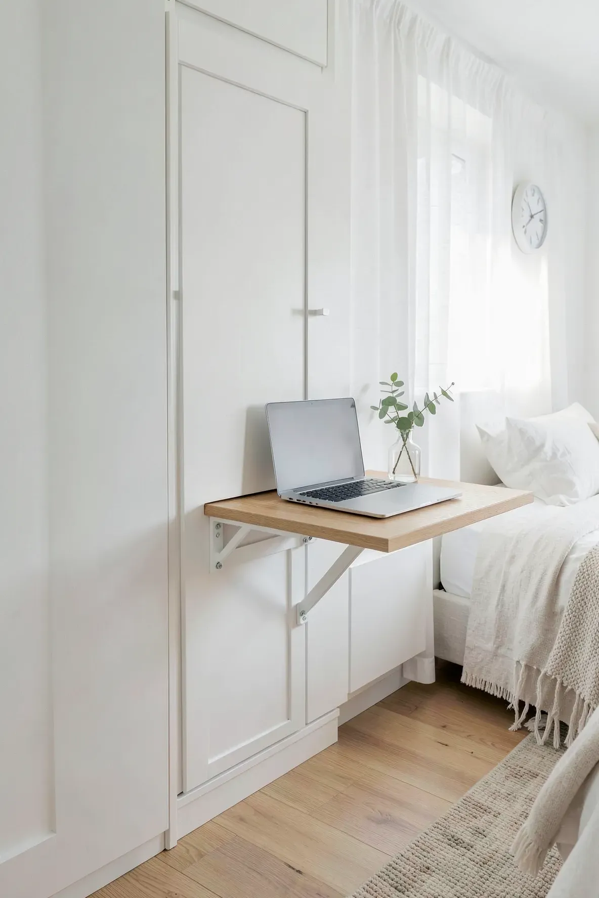 A slim white wardrobe in a bright room featuring a wooden fold-away desk leaf and a laptop.