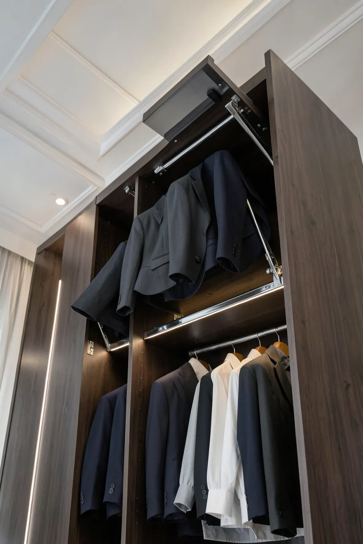 A high-ceiling wardrobe featuring a chrome pull-down lift system for accessing upper clothing rails.