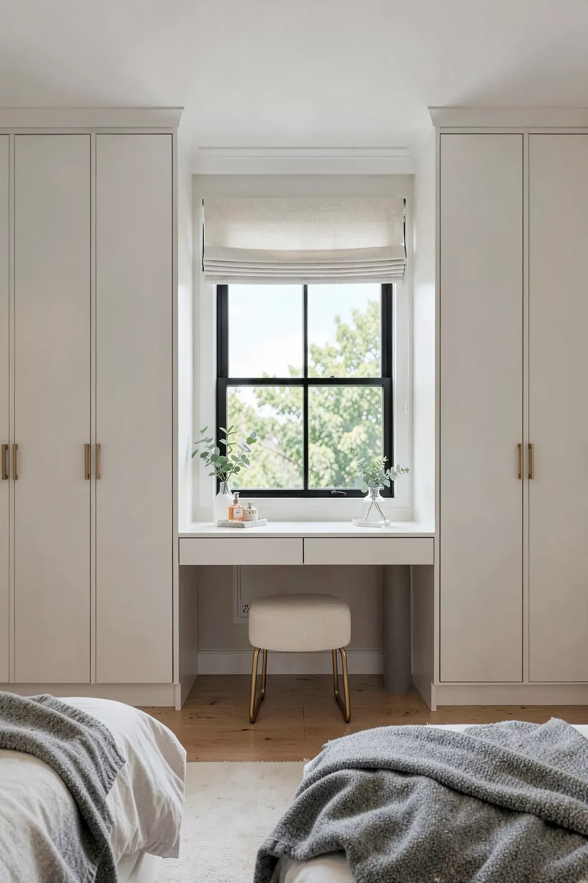 A white built-in wardrobe system with a central vanity desk placed directly under a bright bedroom window.