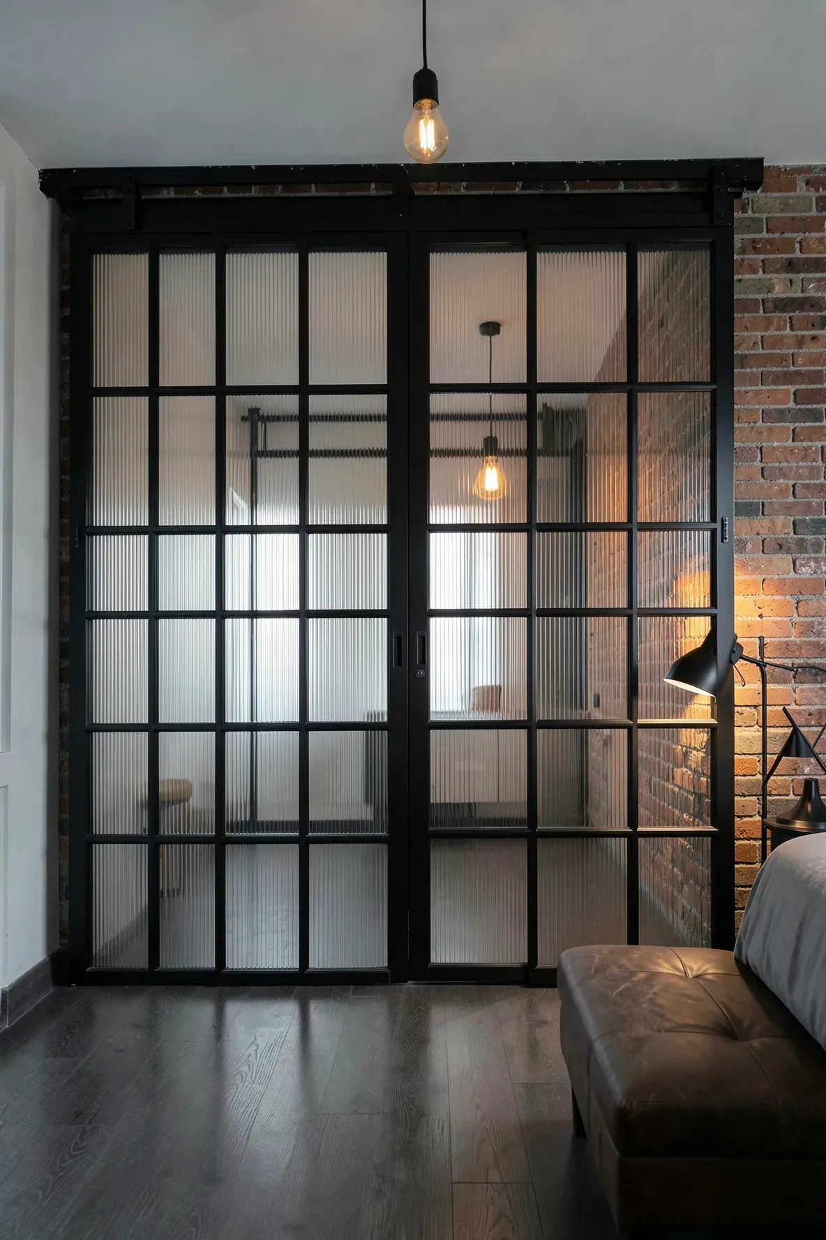 Industrial black grid sliding wardrobe doors with fluted glass in a brick-walled loft.