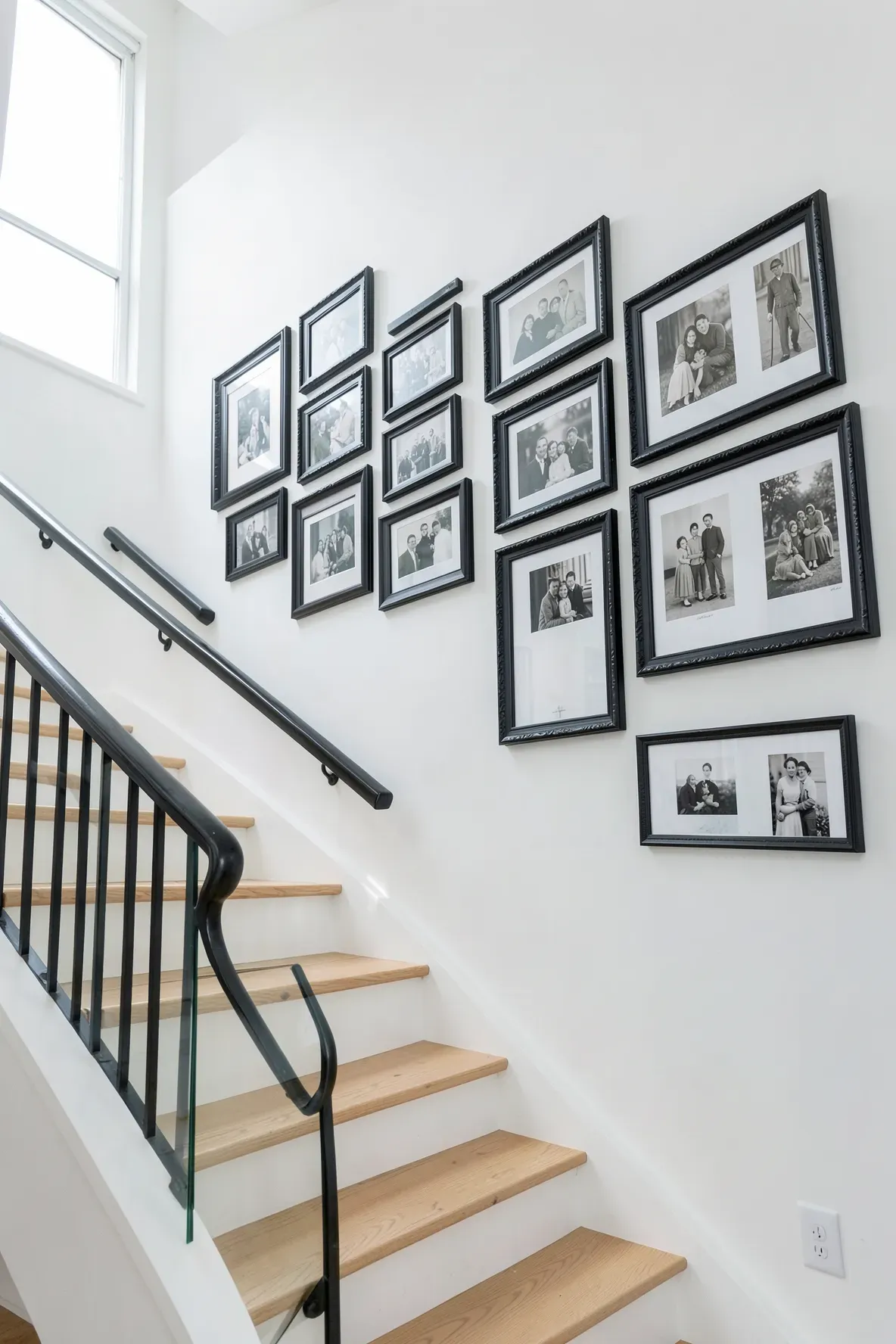 A staircase wall featuring a grid of black and white family photos in matching black frames.