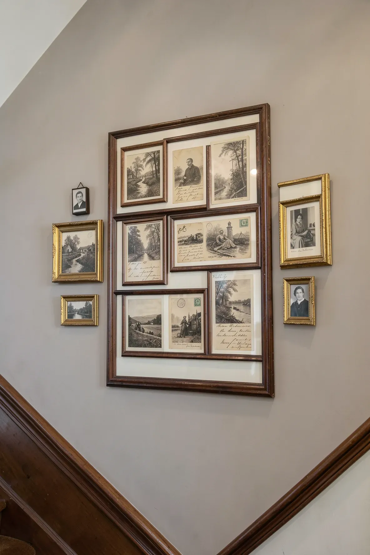 Antique postcards displayed in a multi-window walnut frame on a classic staircase wall.