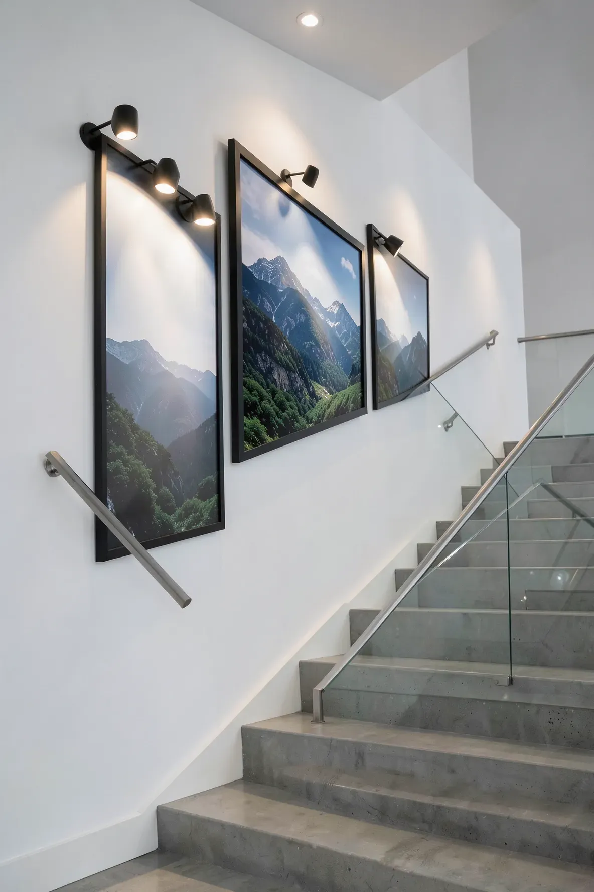 A three-piece landscape triptych following the stairs, lit by individual black picture spotlights.