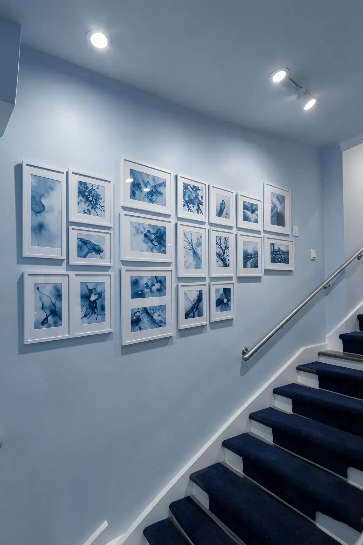 A monochromatic blue art gallery on a staircase wall lit by soft, dimmable ceiling wall washers.