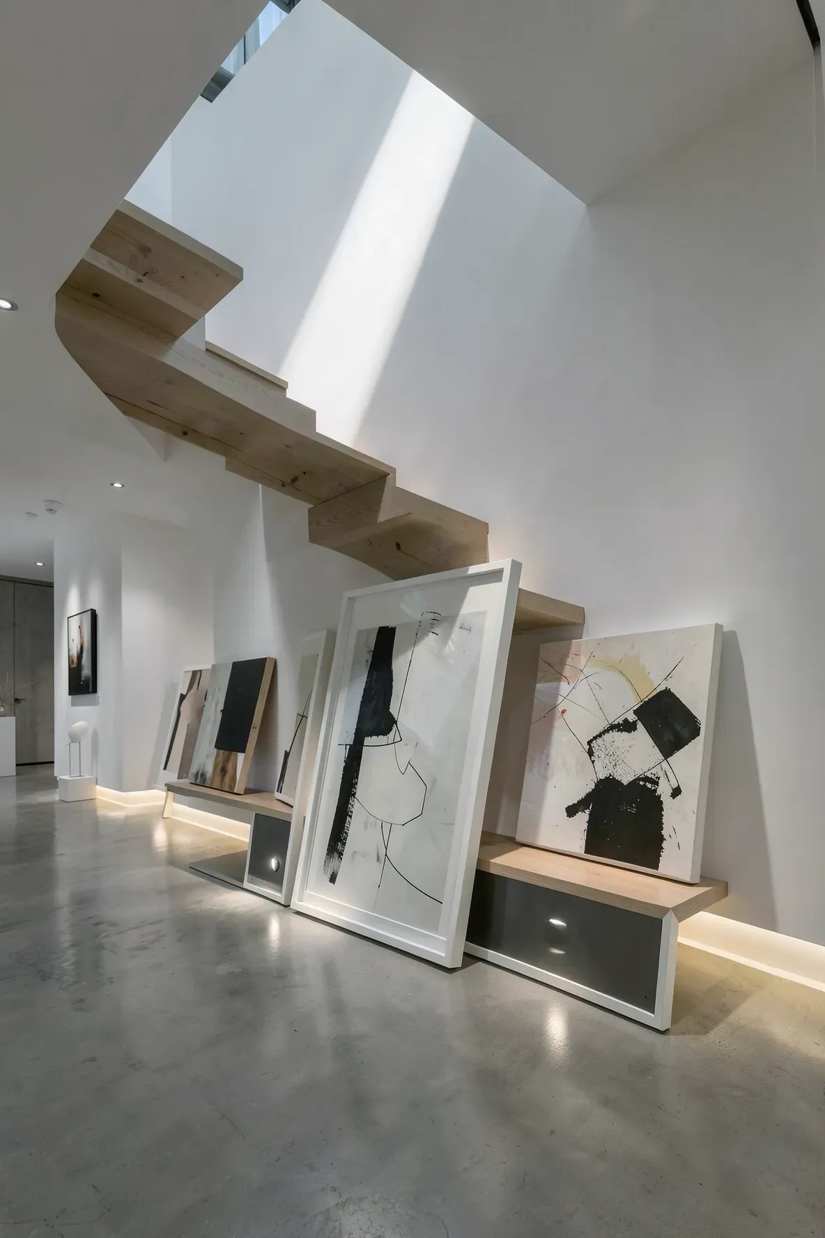 Large art frames leaning against a stairwell wall illuminated by upward-facing floor lights.