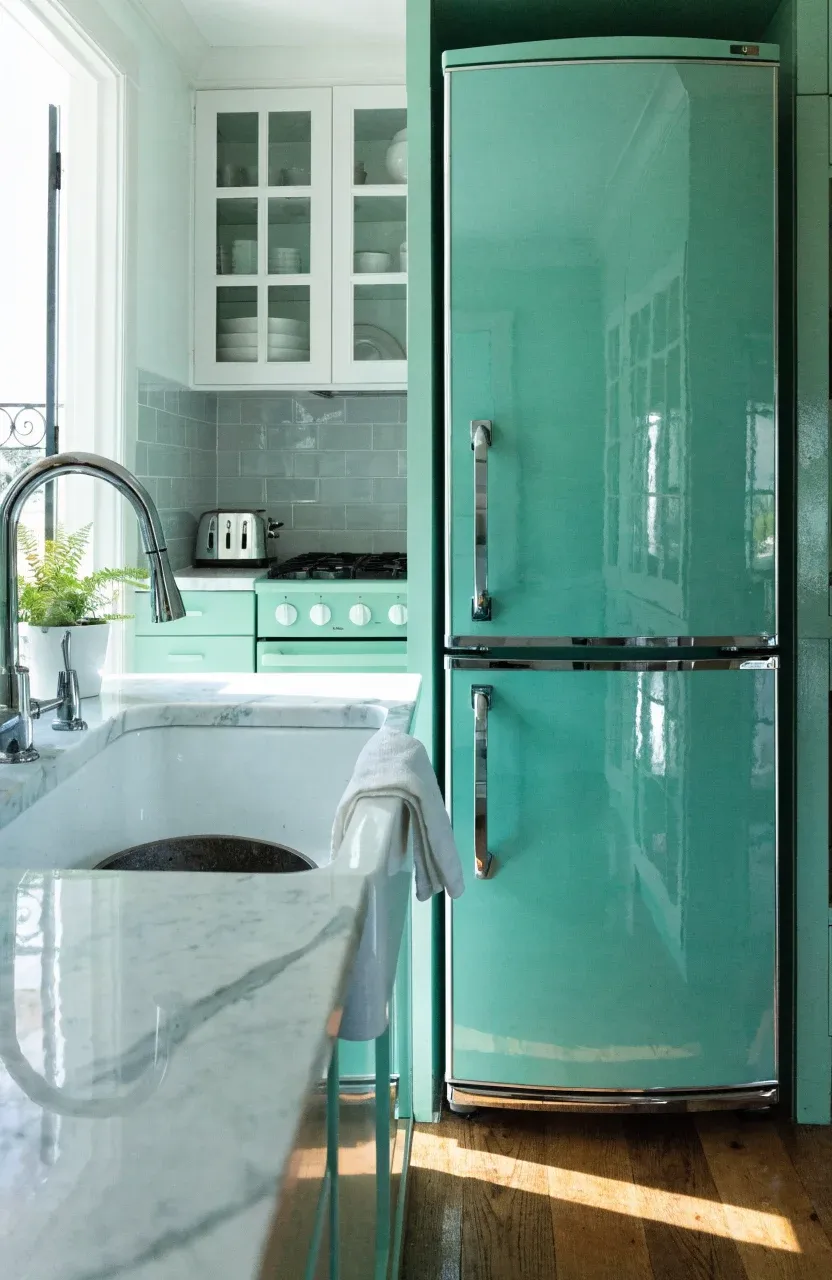A mint green slimline refrigerator and a deep farmhouse sink in a small, well-designed kitchen.