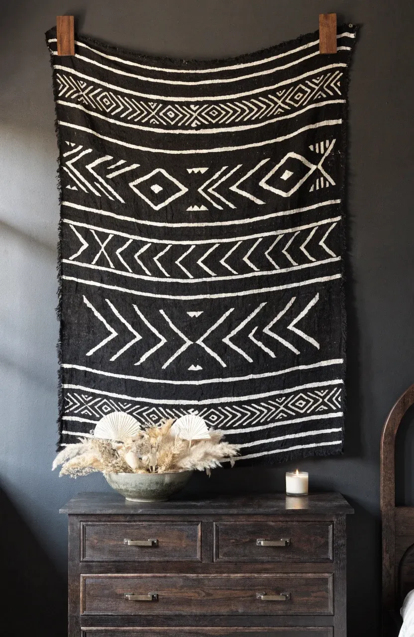 A black and white mudcloth tapestry hung with dark wood clips on a dark bedroom wall.