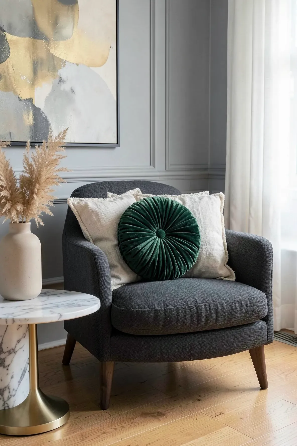 A round emerald green velvet pillow with a center button on a grey armchair in a modern room.