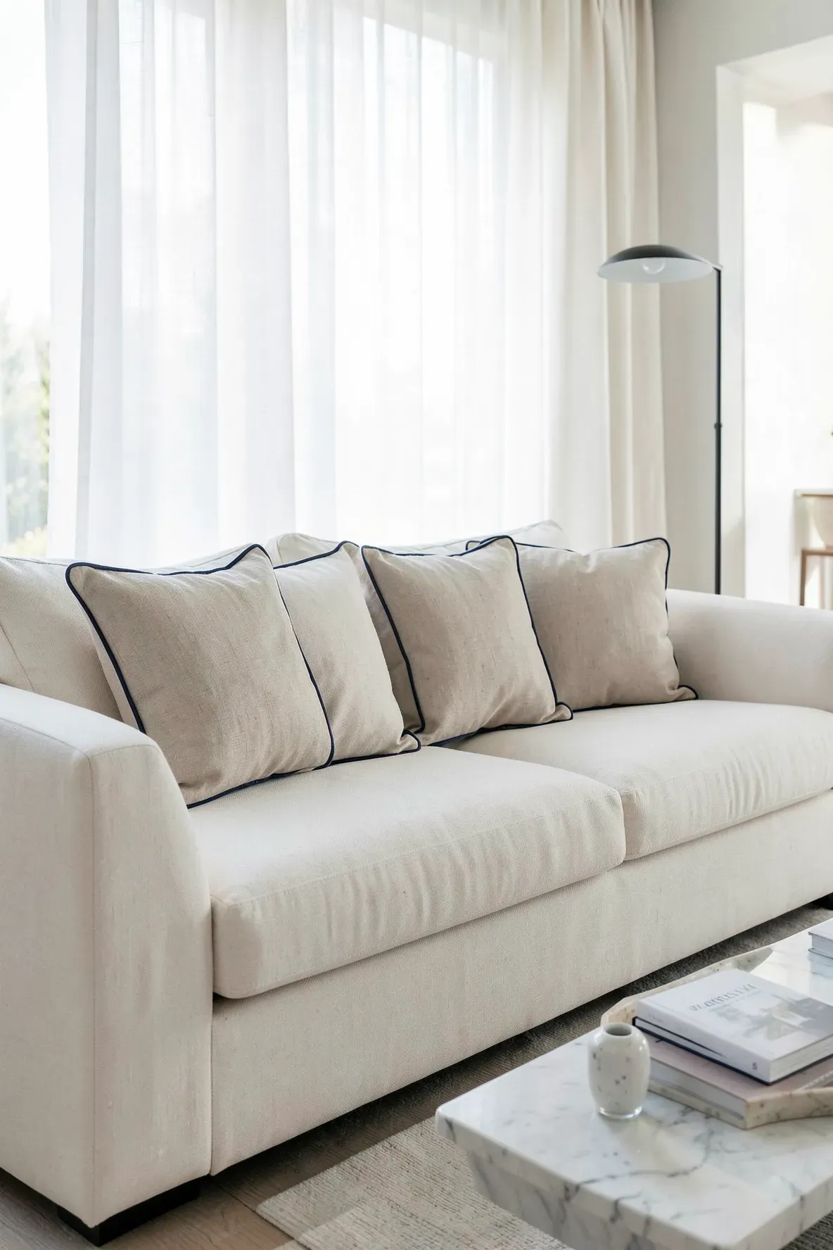 Oatmeal linen pillows with navy blue piping arranged on a cream sectional sofa.