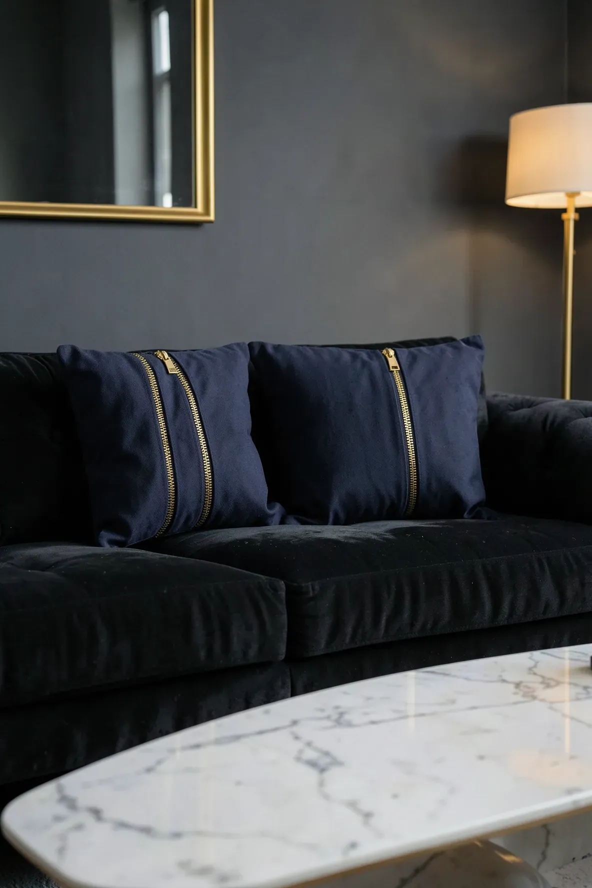 Navy blue pillows with decorative gold metal zippers on a charcoal velvet sofa.