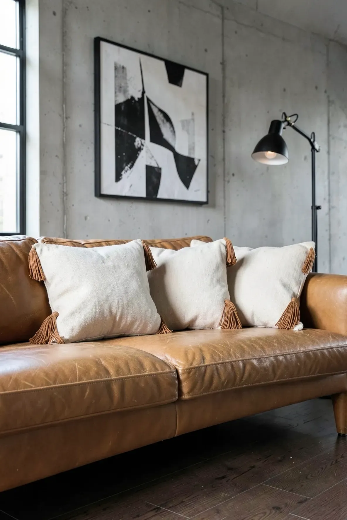 Cream canvas pillows with cognac leather tassels on a leather sofa.