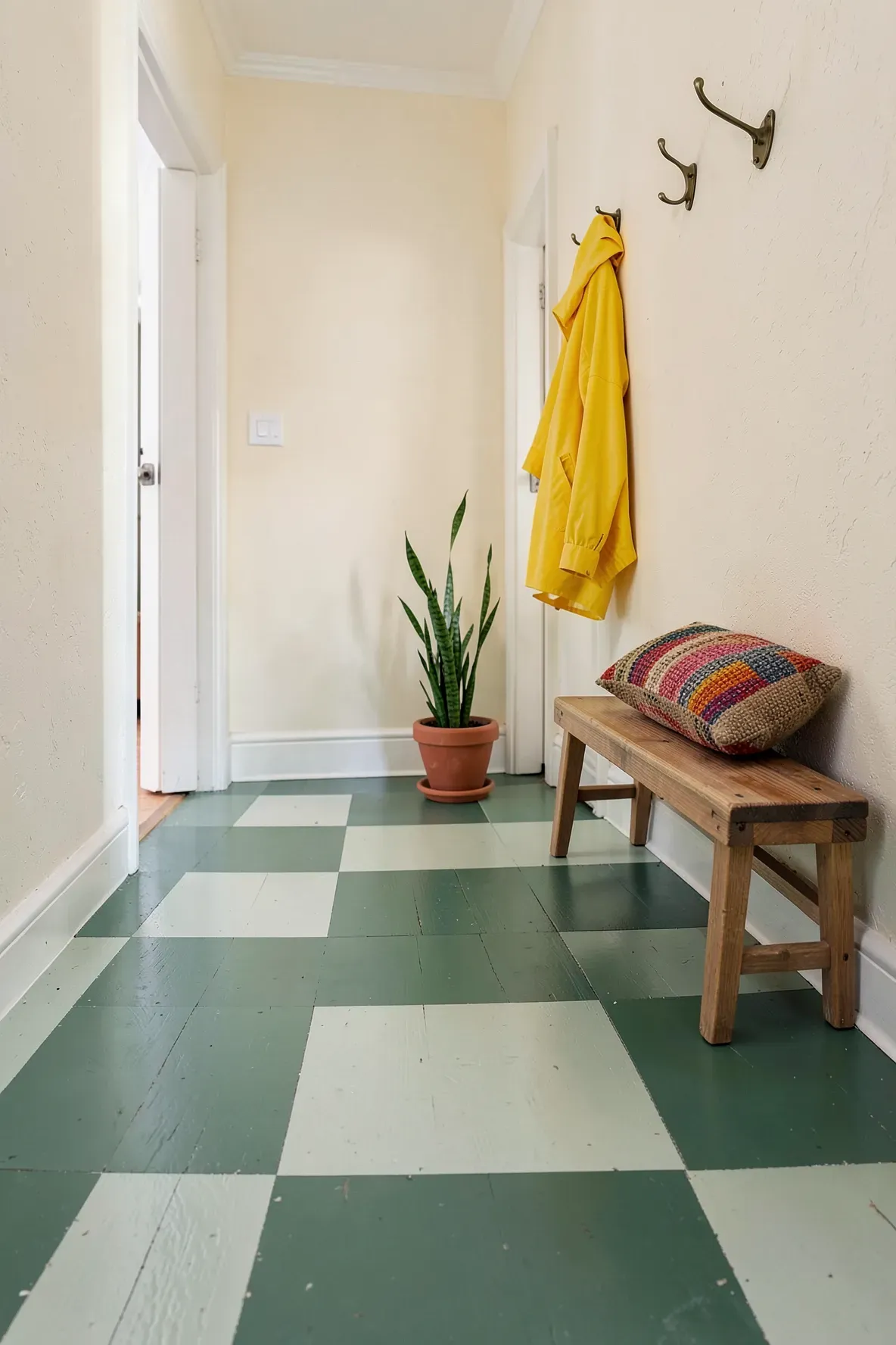 A small entryway featuring a sage green checkerboard painted wood floor and a simple oak bench.