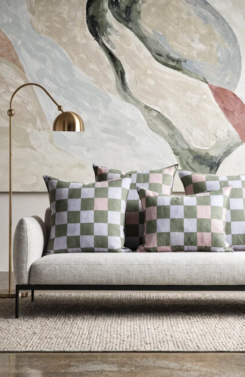 Sage green and dusty rose checkerboard pillows arranged on a modern grey sofa.
