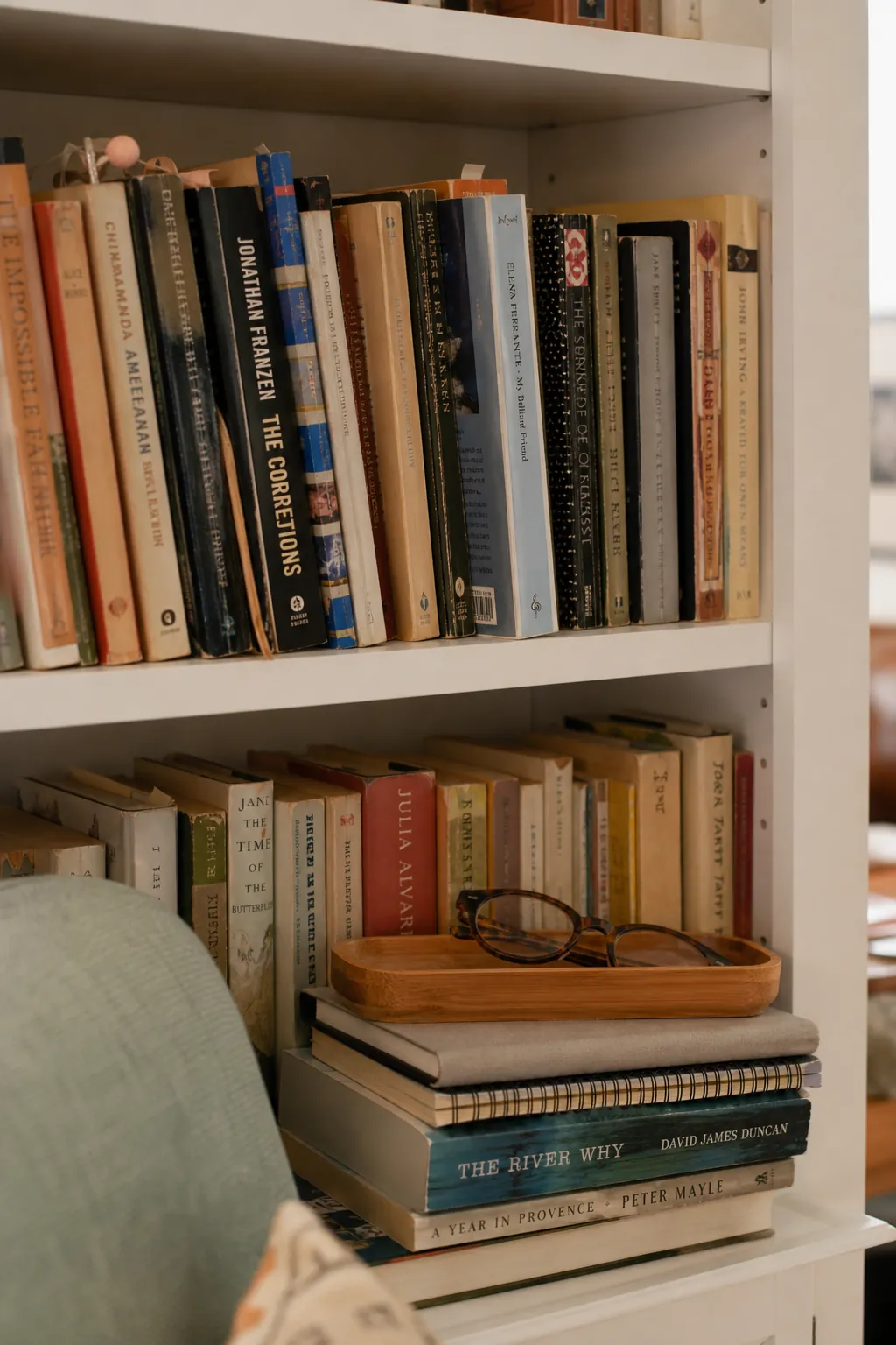 A lived-in bookshelf with real books, notebooks, and a small bamboo tray in a cozy reading nook