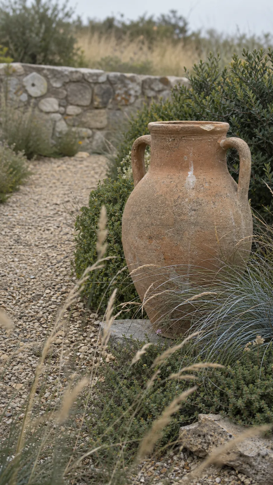 Weathered clay amphora nestled among soft ornamental grasses