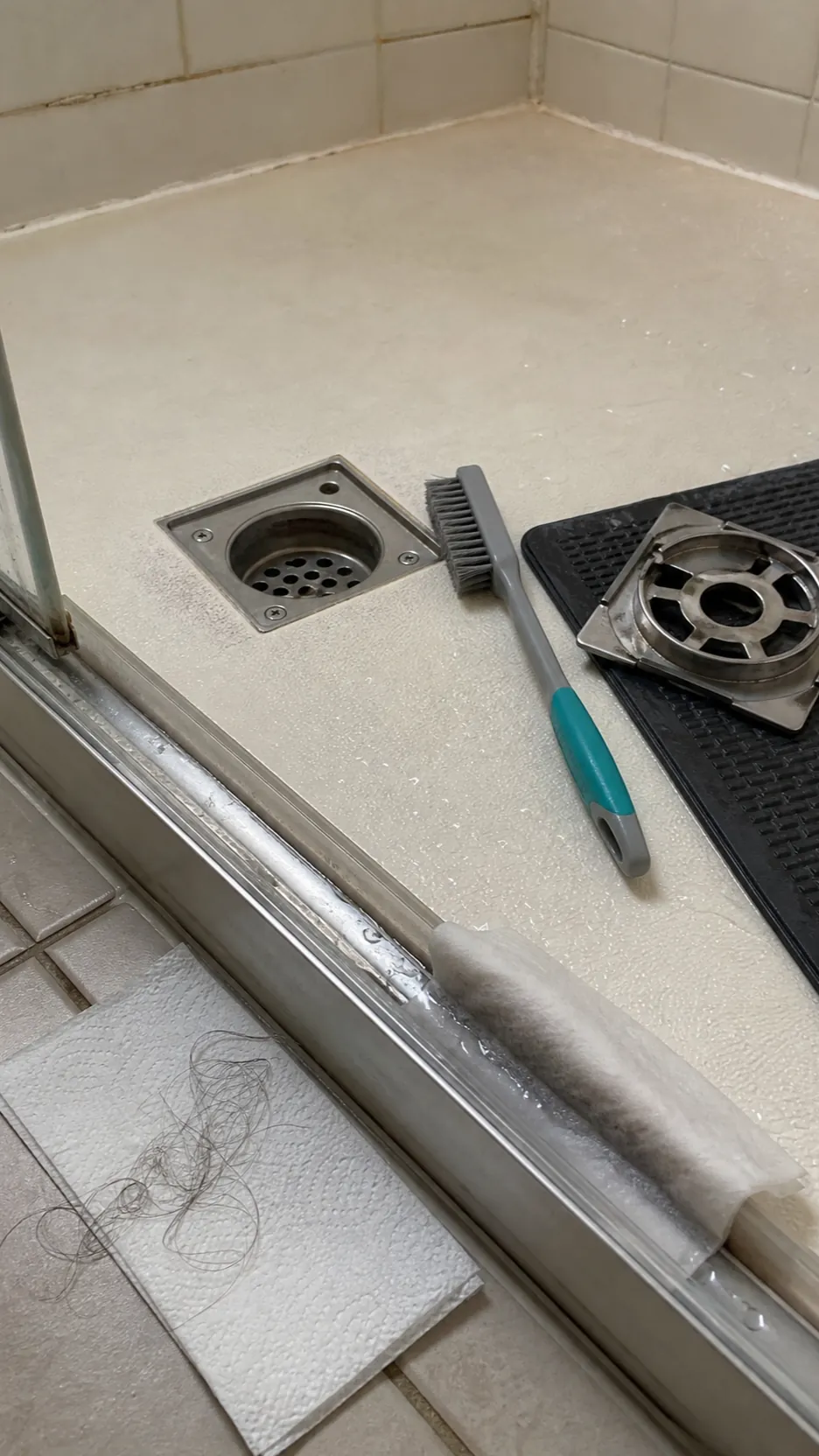 Detail cleaning around a shower drain and sliding door track with a soft brush