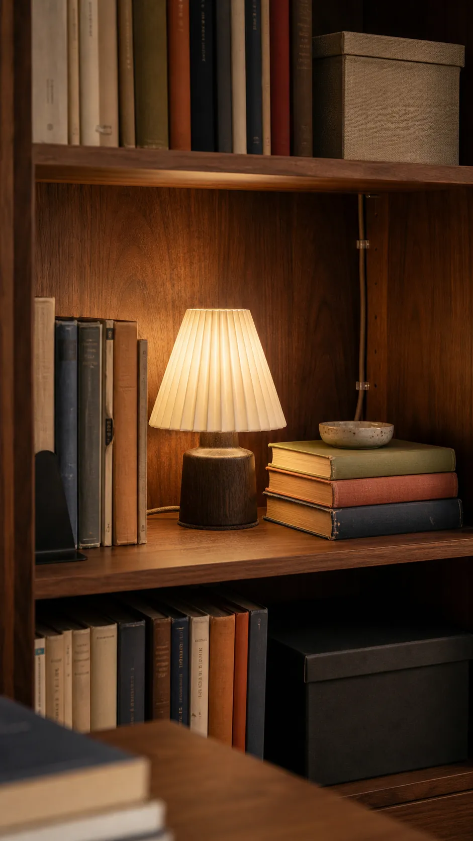 Small pleated lamp styled between book stacks on a warm wood shelf