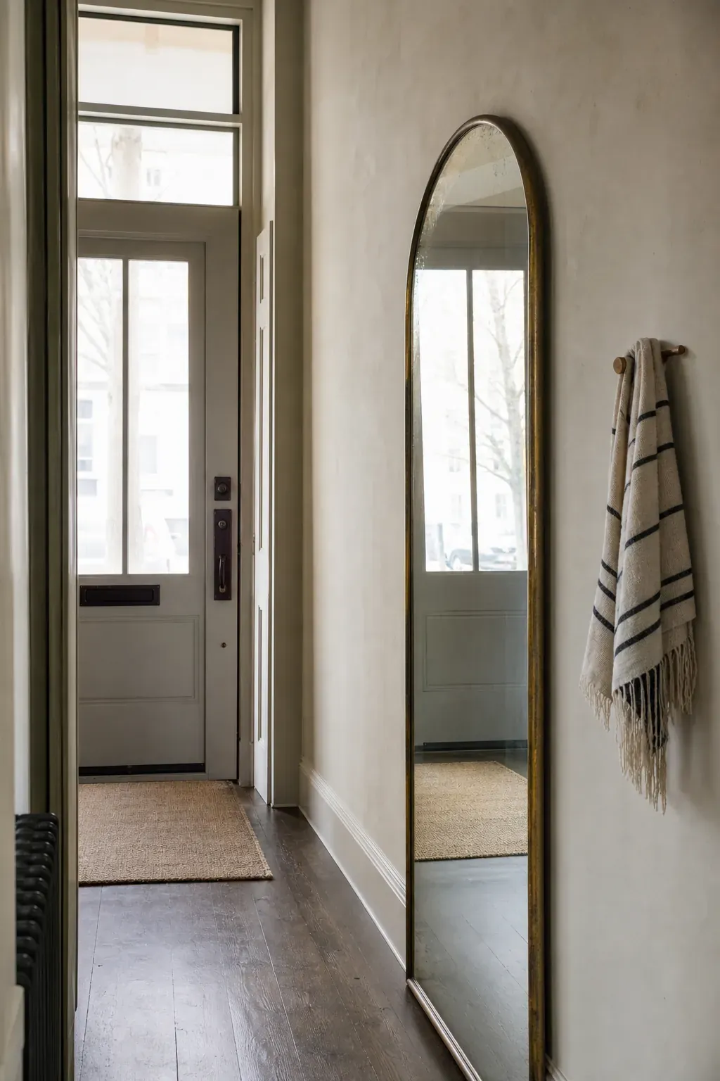 Tall mirror reflecting daylight through a narrow entrance hall
