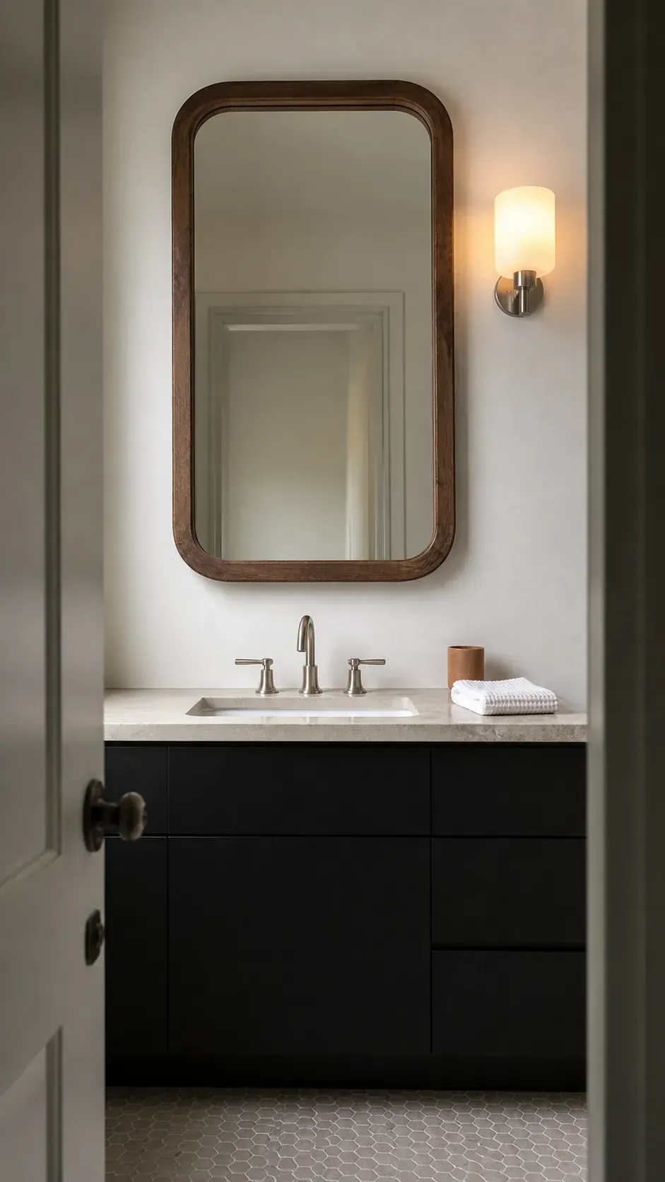 Black bathroom vanity beneath a rounded walnut framed mirror