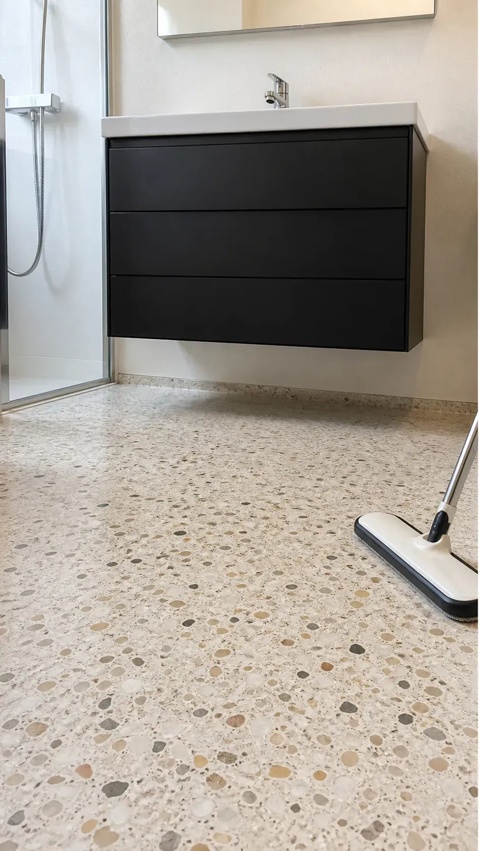Floating black vanity above pale warm terrazzo flooring