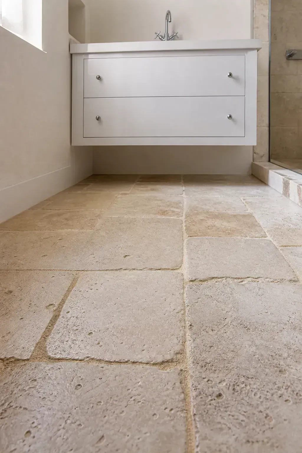 White bathroom vanity over tumbled limestone flooring