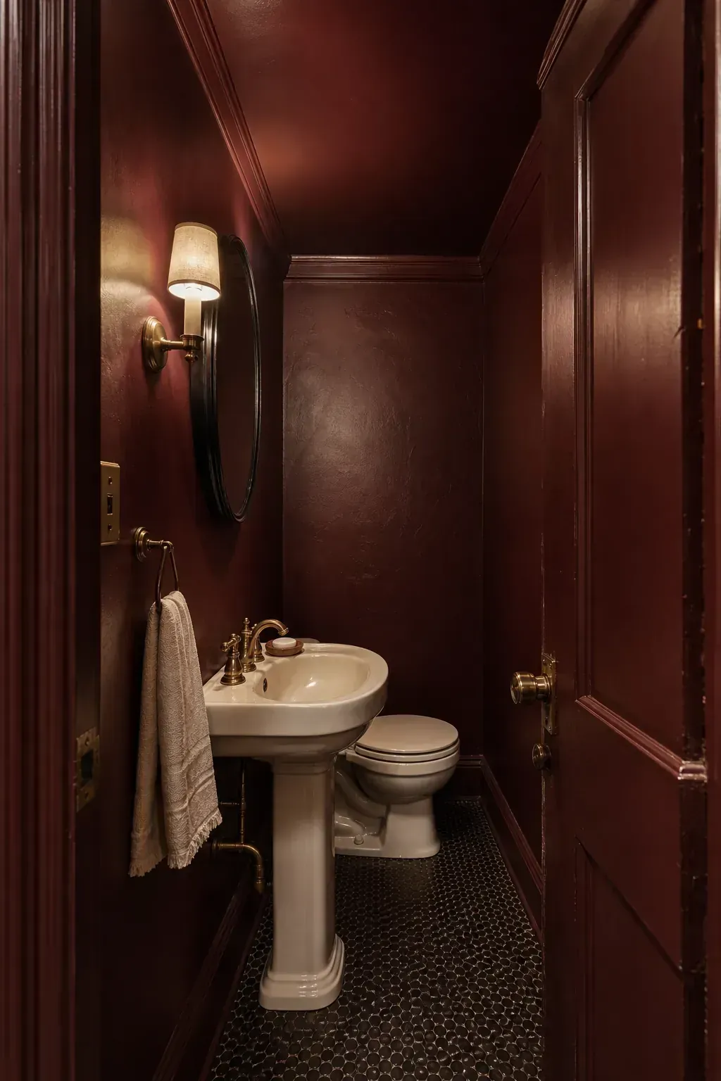 Oxblood color-drenched moody half bathroom with brass fixtures