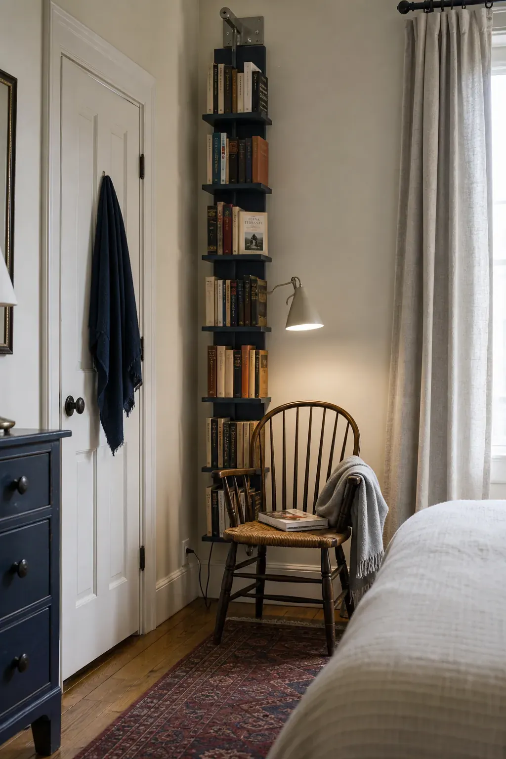 Slim vertical book tower behind a bedroom reading chair