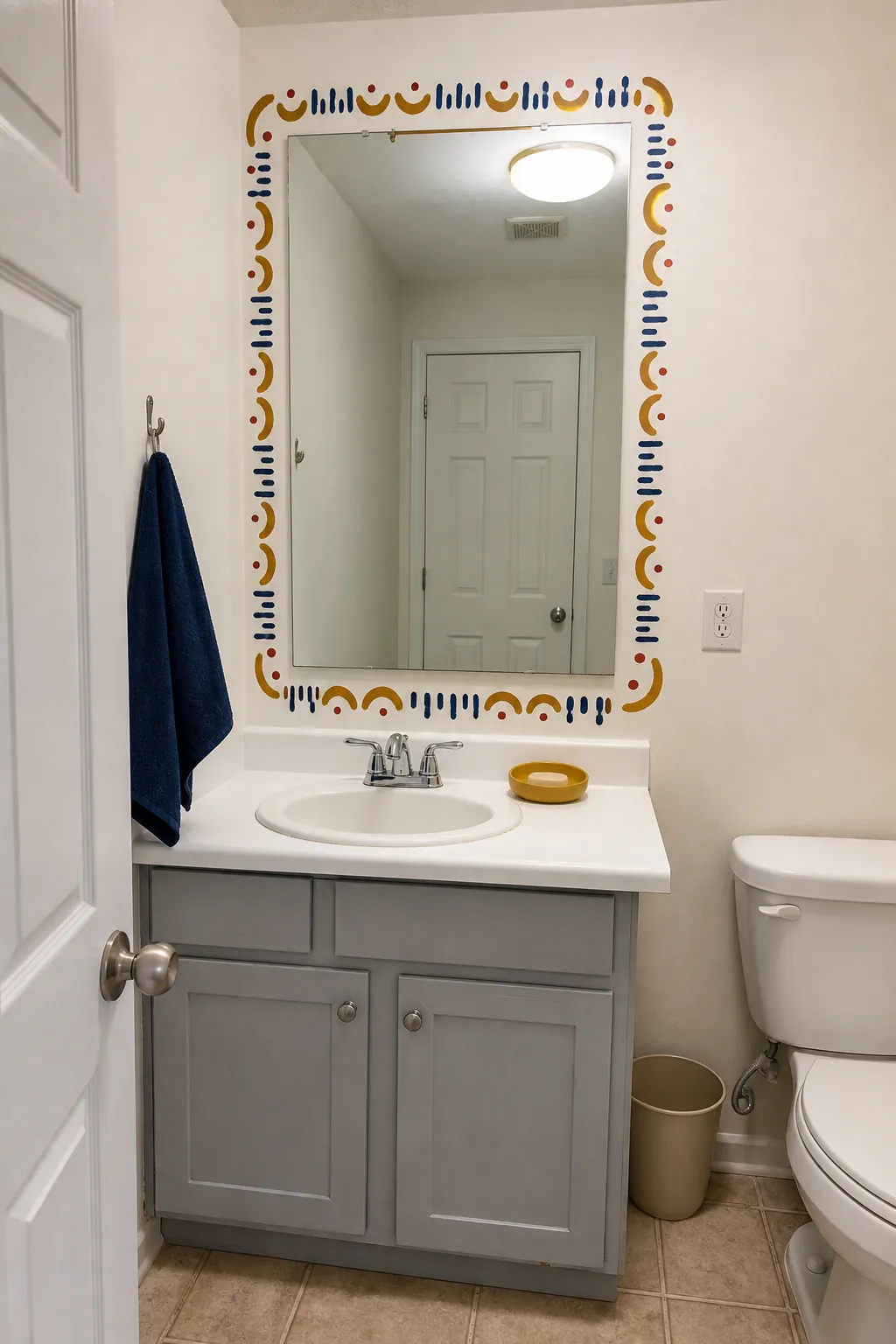 Budget powder room with a hand-painted decorative border around the mirror