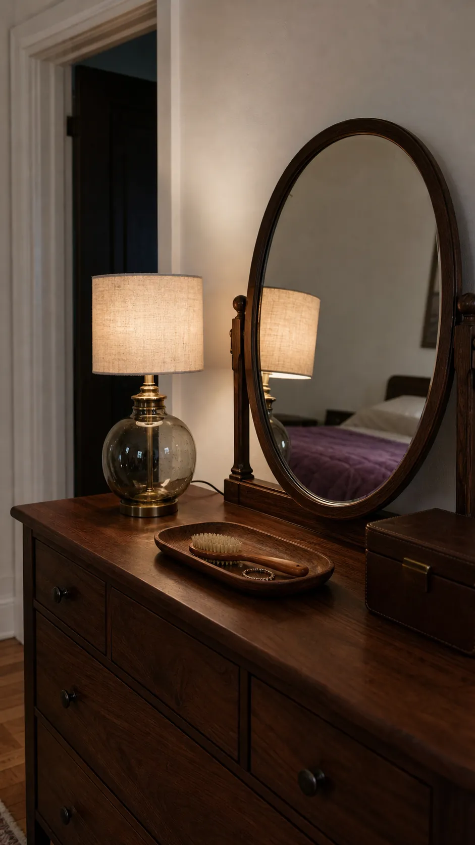 Glass dresser lamp softly reflected in a bedroom mirror