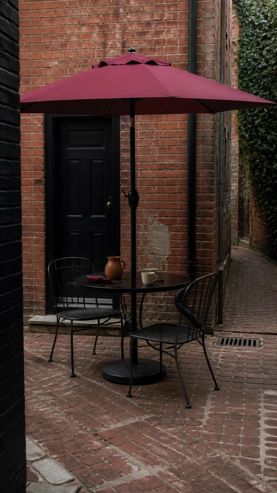 Muted red café umbrella above a small brick patio table