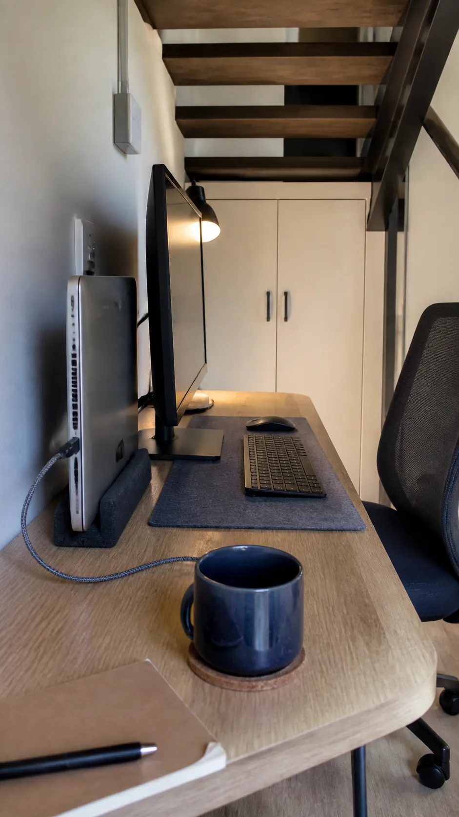 Closed laptop stored upright beside a compact desk monitor