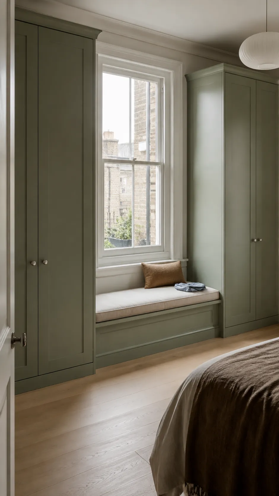 Soft green wardrobes framing a practical bedroom window seat