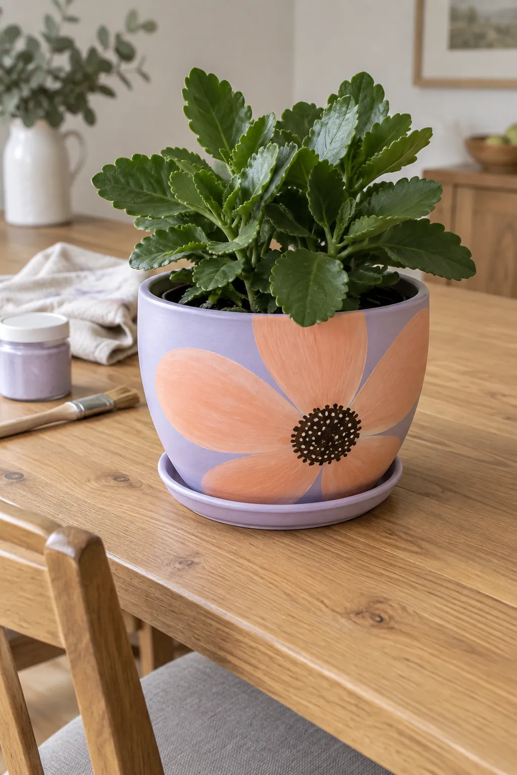 A pale lilac wide flowerpot painted with one oversized peach flower whose broad petals disappear around the sides, holding a compact green kalanchoe