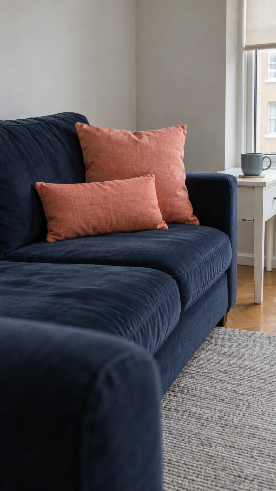 Muted coral cushions warming a navy sofa in a small living room