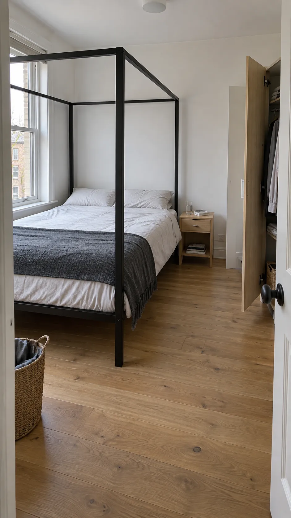 Slim black canopy bed with clear walking space beside a wardrobe