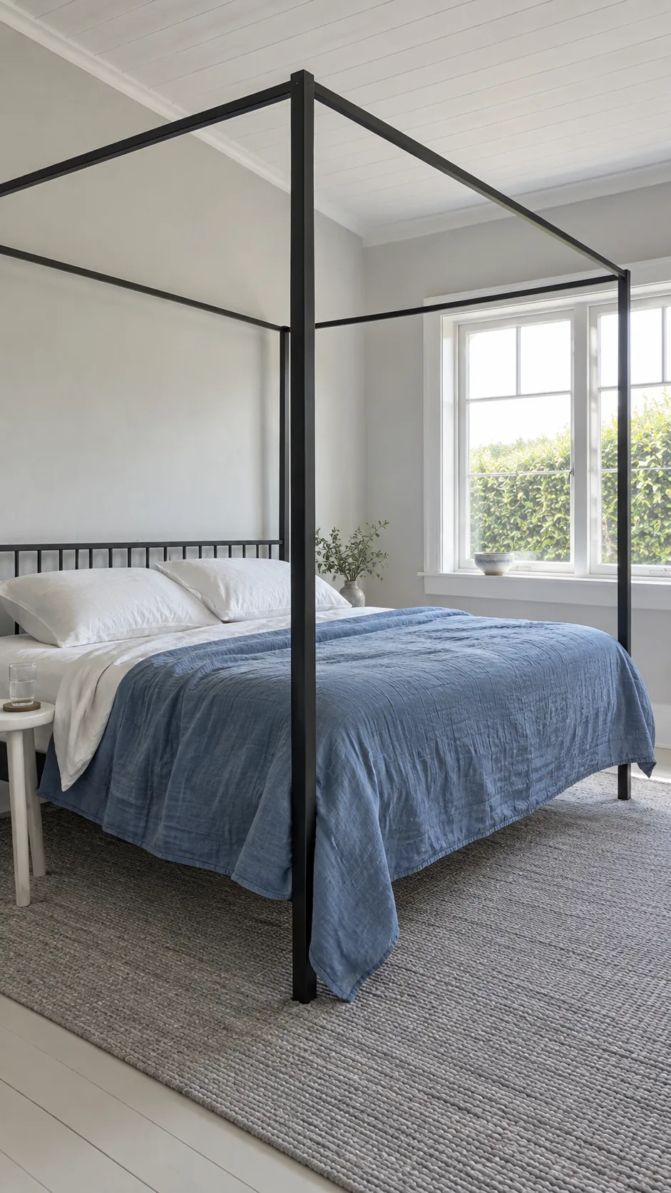 Bare black canopy frame with blue bedding in a bright bedroom