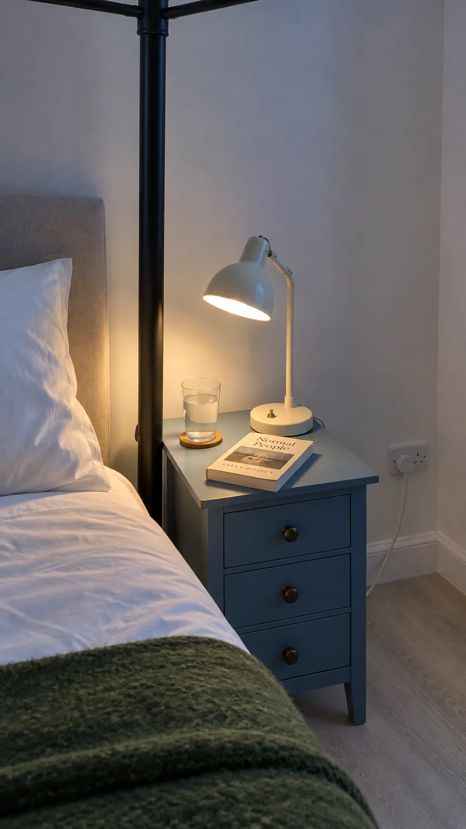 Reachable reading lamp and nightstand beside an iron canopy bed