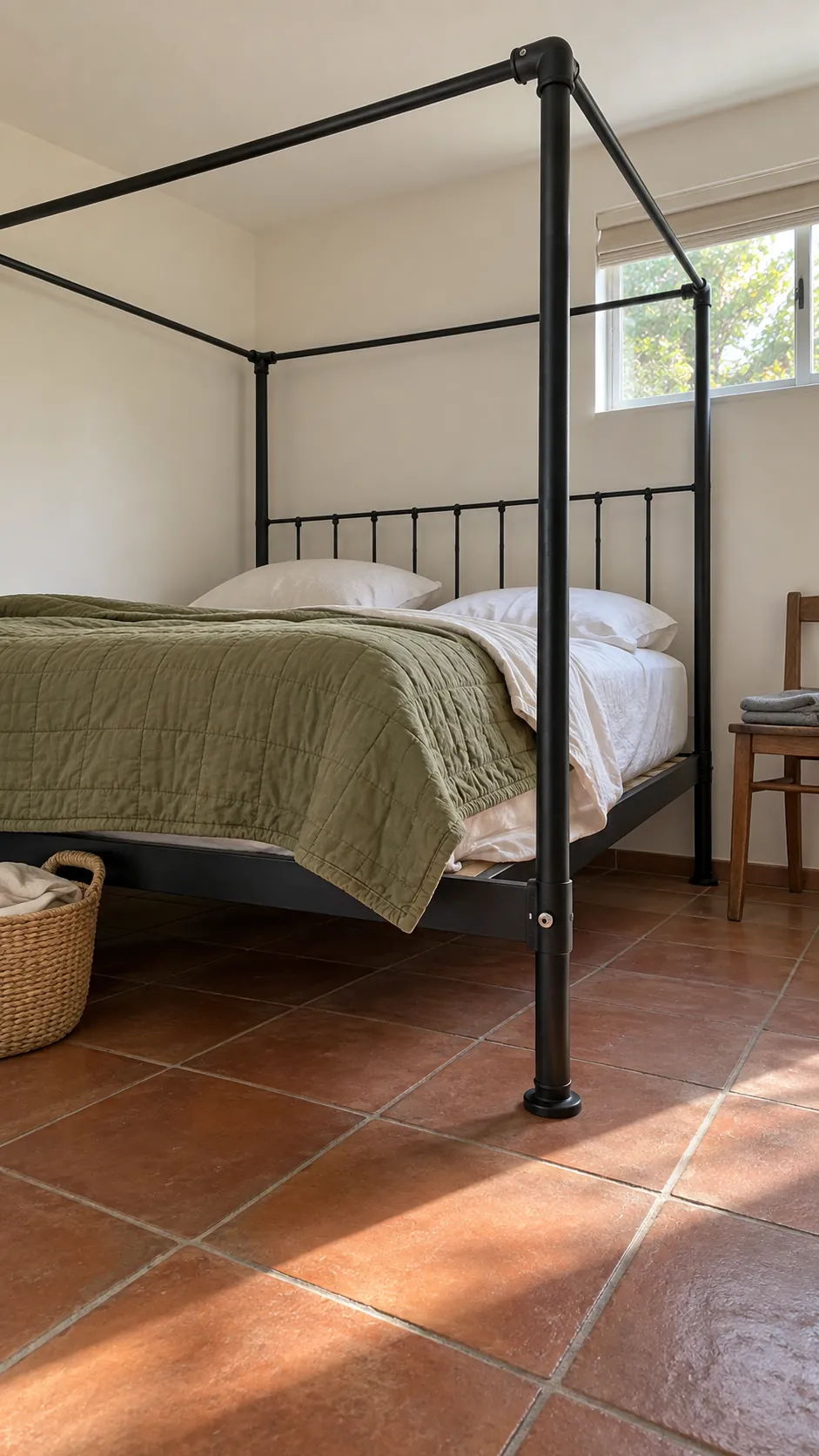 Black iron canopy bed with visible joints and simple olive bedding