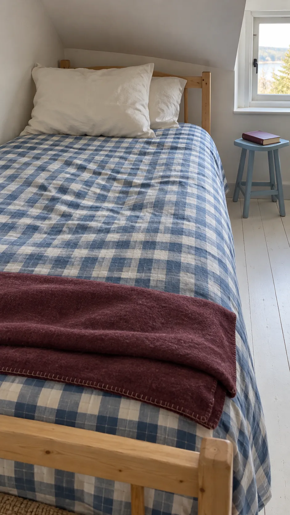 Blue checked coverlet on a simple bed with plain pillows and a folded blanket