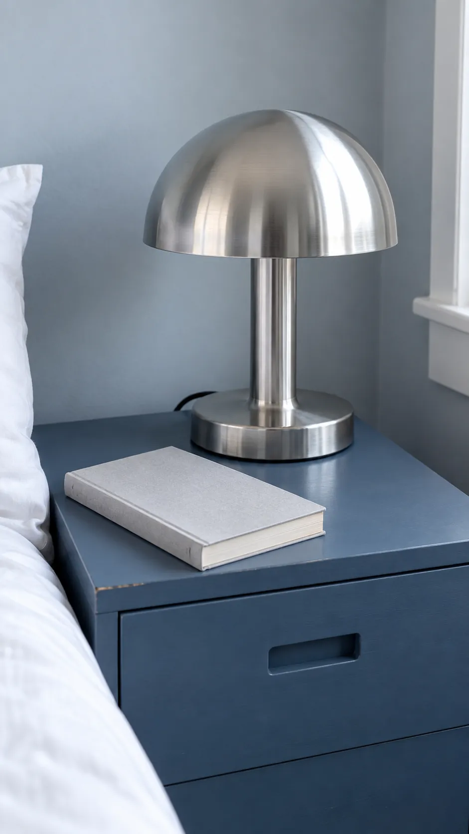 Chrome bedside lamp reflected against a matte blue cabinet