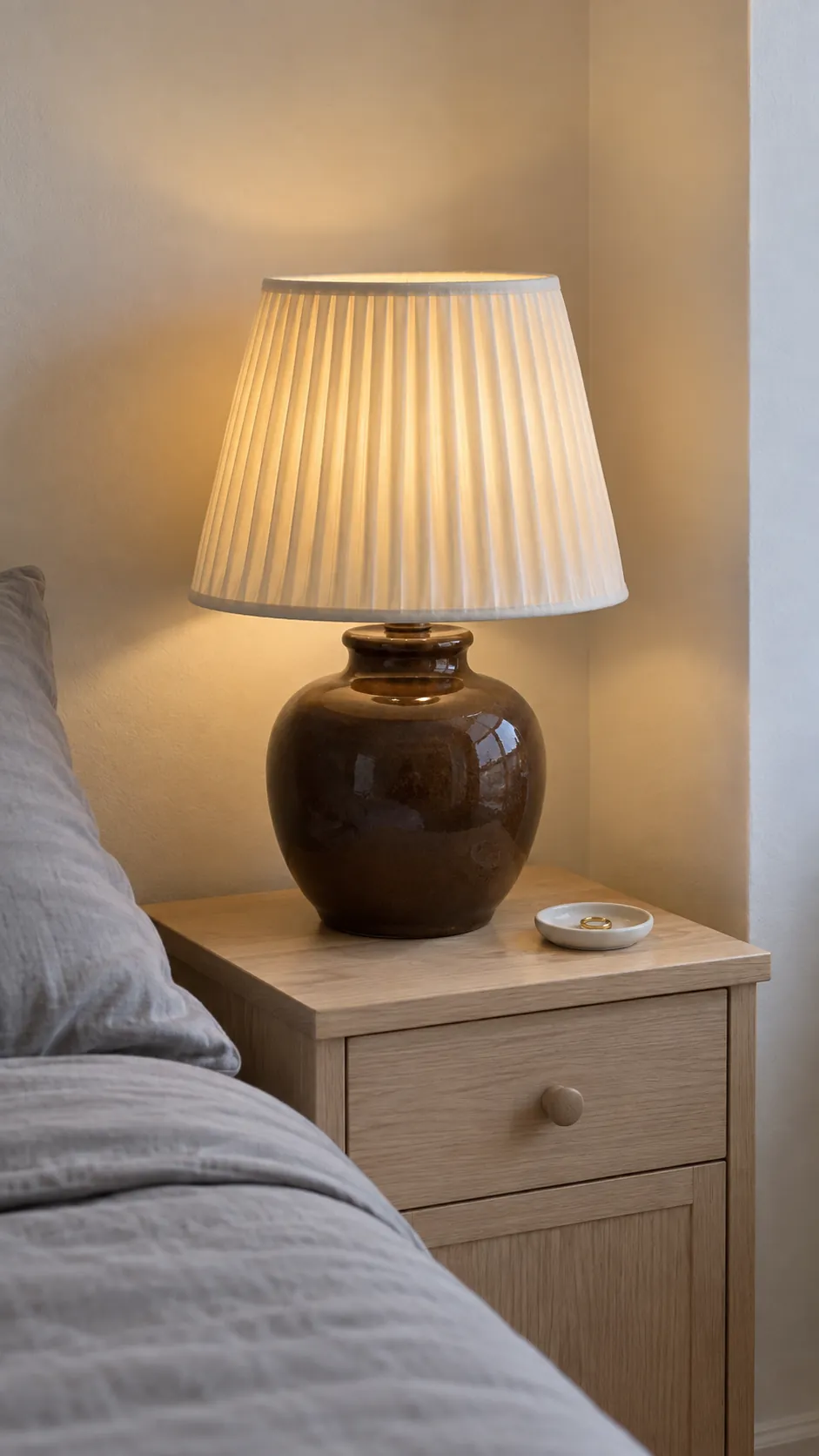 Pleated ivory lampshade on a brown ceramic lamp in a bedroom corner