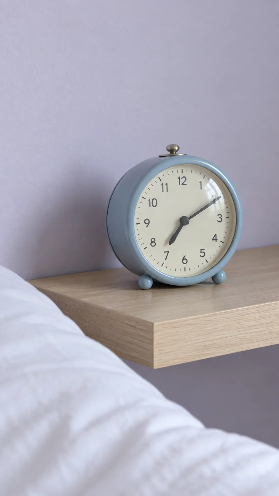 Muted blue enamel alarm clock on a small bedside shelf