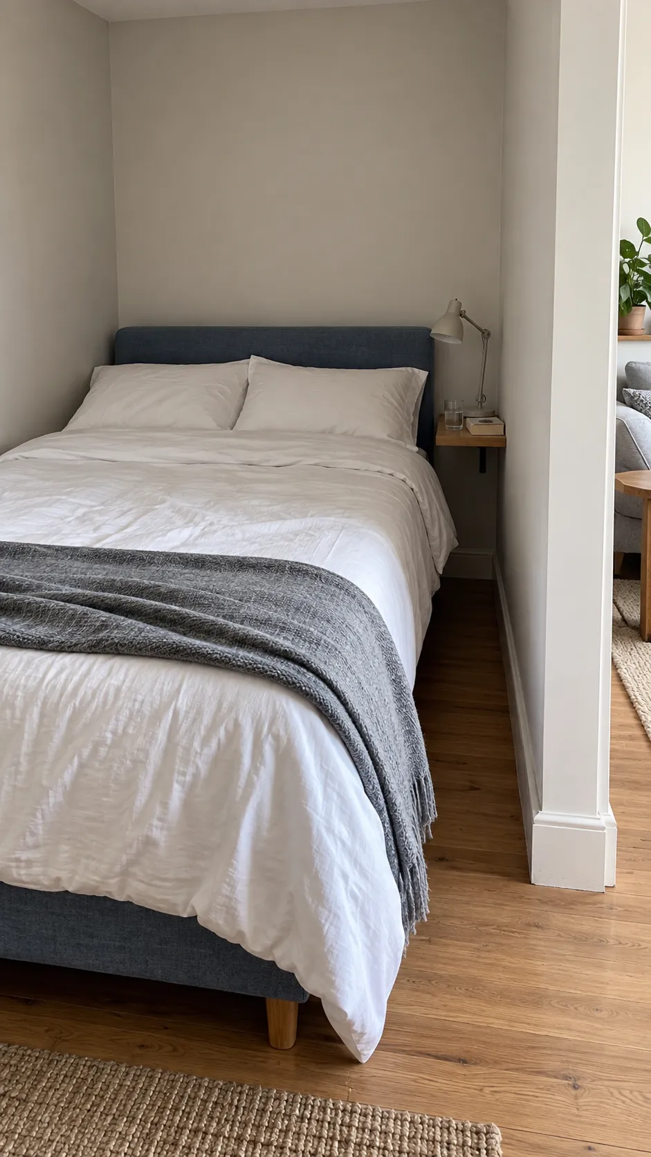 Create a credible photograph of a sleeping alcove in a studio, emphasizing how a bed can occupy a quieter side of the room while preserving a useful approach