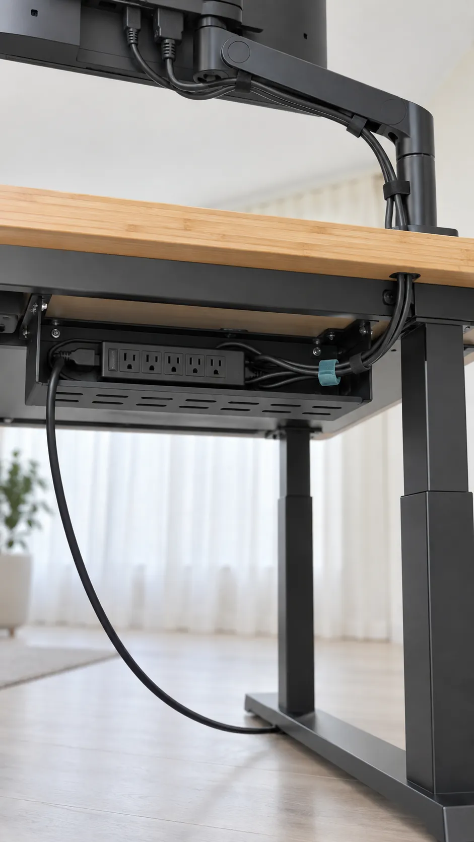 Capture the relaxed cable path beneath a standing desk and along a monitor arm, showing useful slack as an ordinary physical detail rather than a decorative cable management showcase