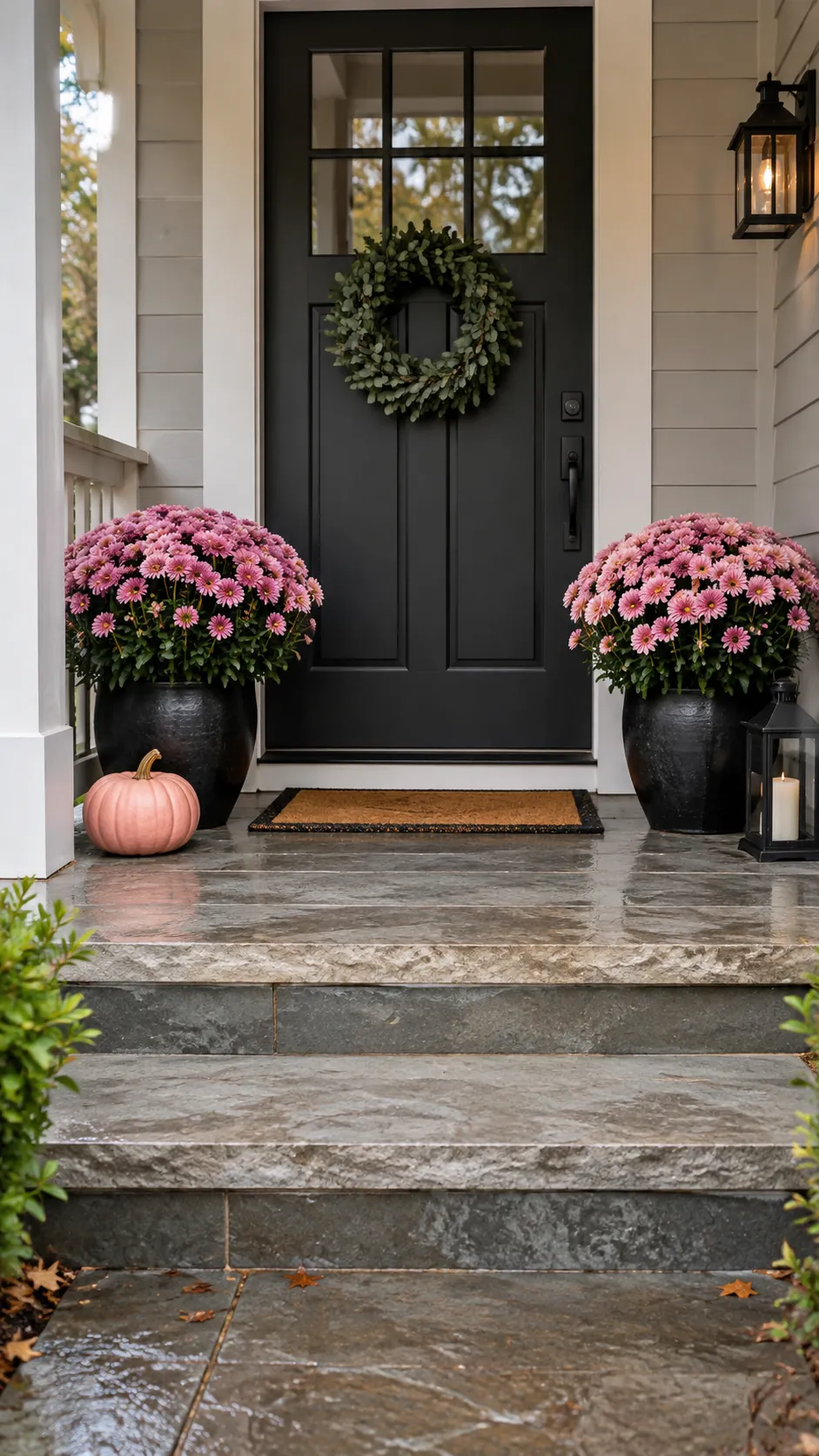 Pink and black Halloween decor with pink chrysanthemum blooms in two black planters with one low pumpkin at a pot base